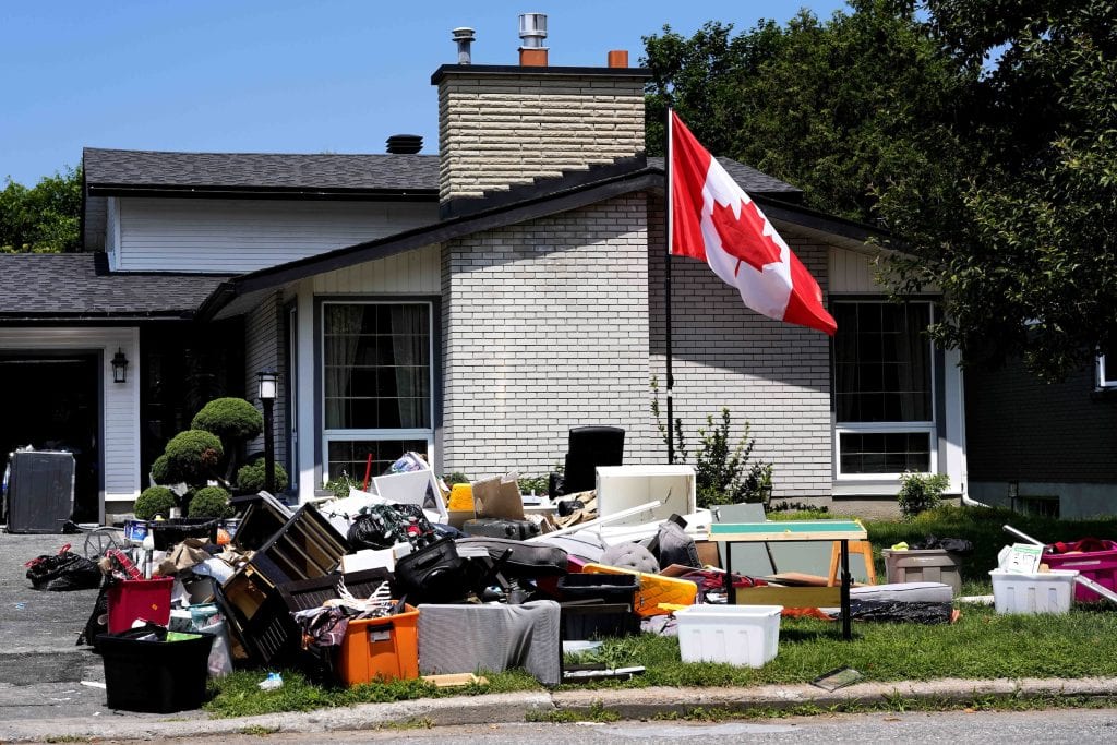 Flood-damaged furniture and other belongings sit on the front lawn of a house, which also sports a Canadian flag flying on a pole.