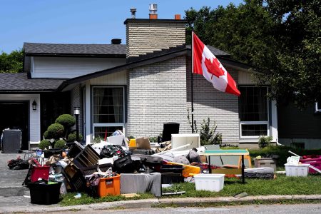 Flood-damaged furniture and other belongings sit on the front lawn of a house, which also sports a Canadian flag flying on a pole.