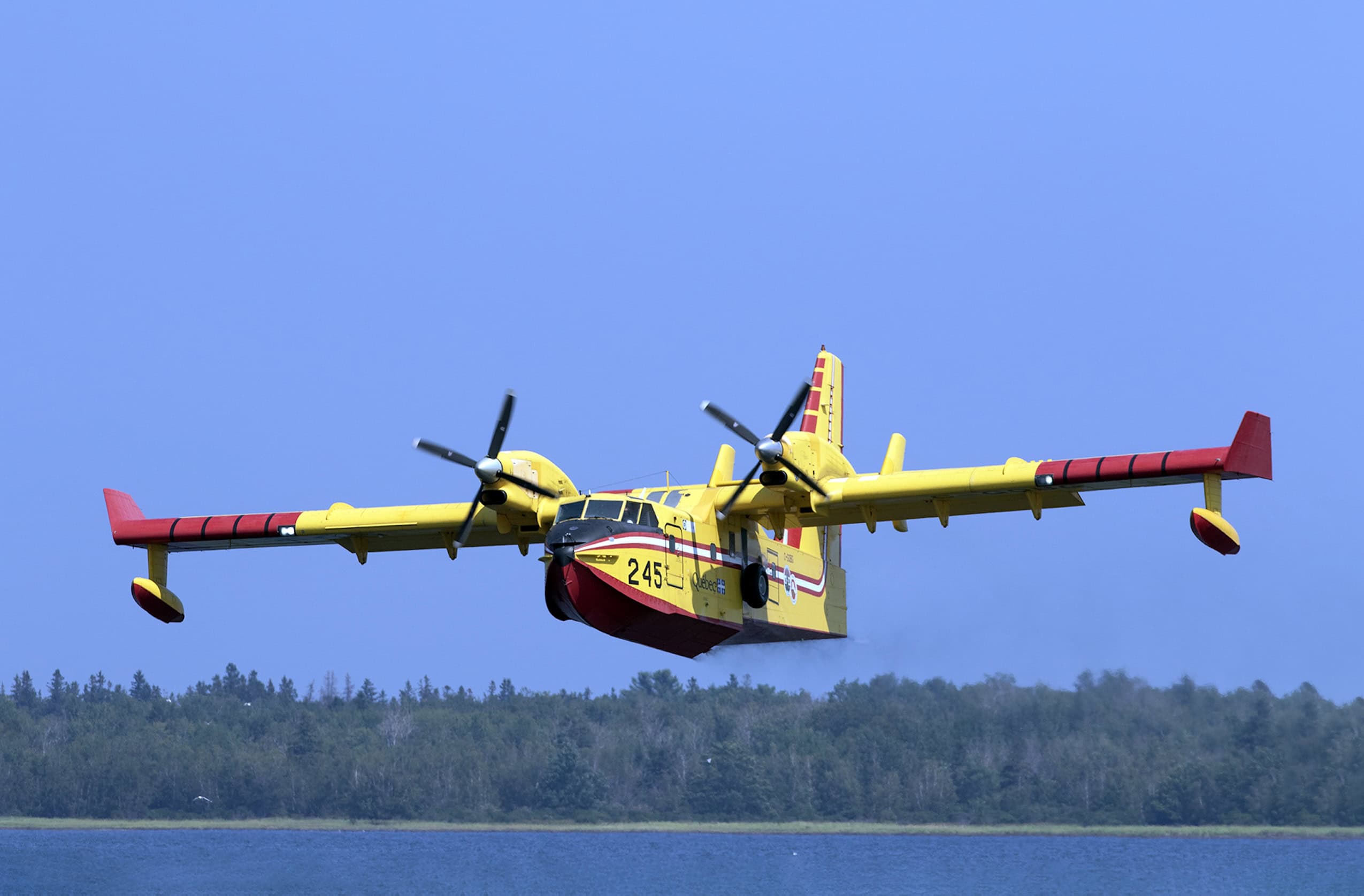 A red and yellow water bomber aircraft flies low over a body of water.