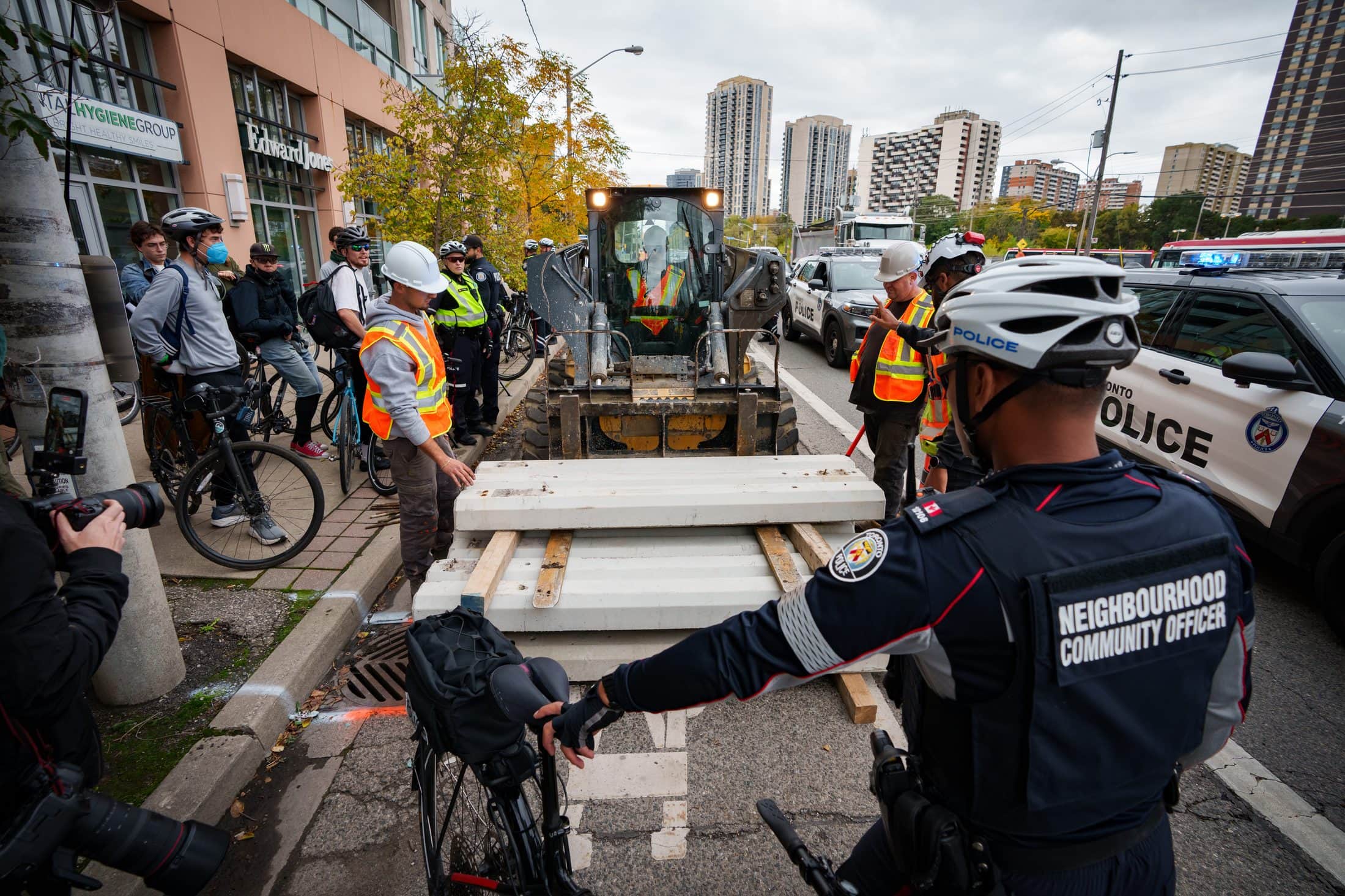 A construction vehicle is on a bike lane with police and climate protestors gather around it