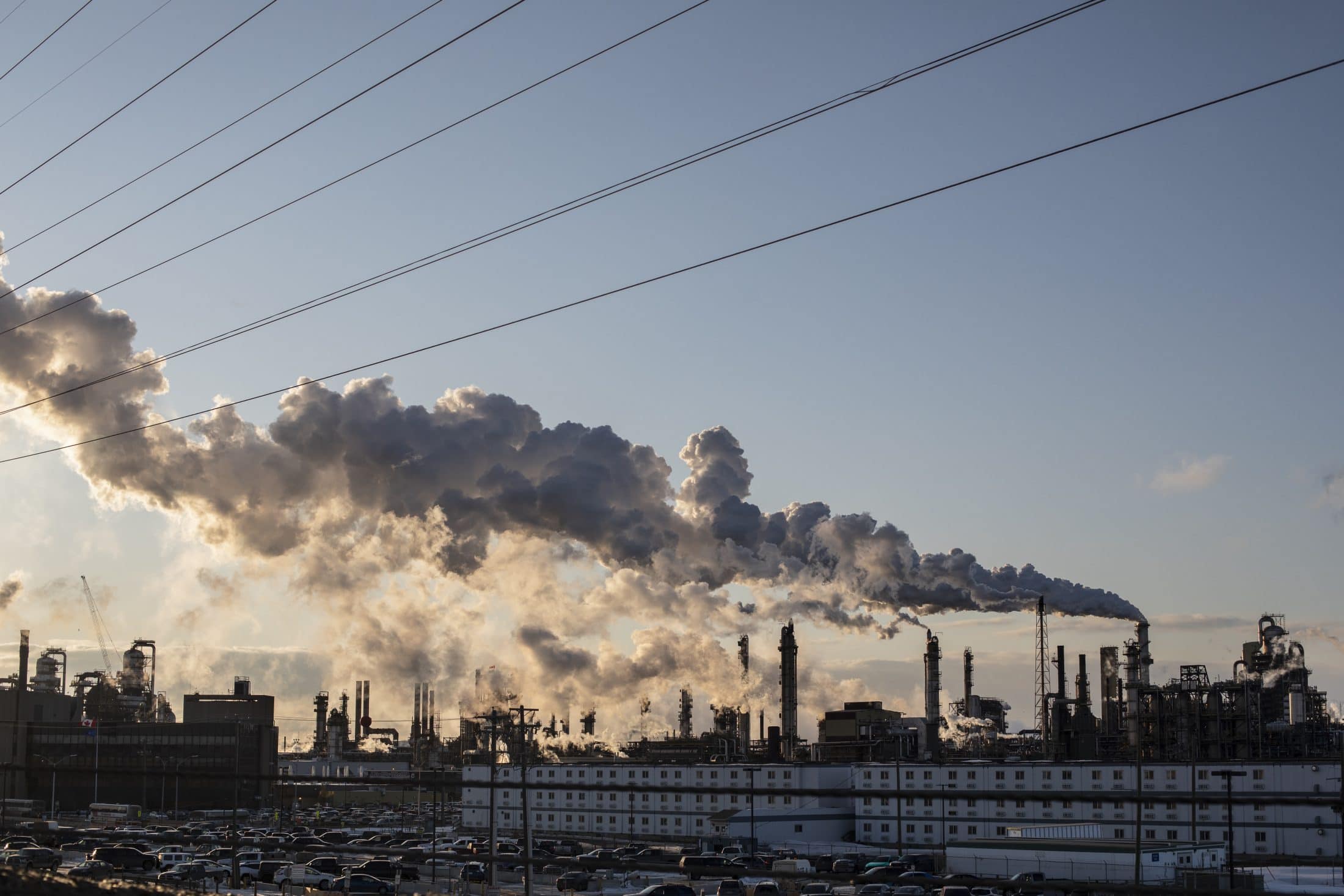 Plumes of emissions from a synthetic crude oil production facility billow into an otherwise clear, blue sky.