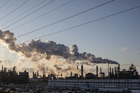 Plumes of emissions from a synthetic crude oil production facility billow into an otherwise clear, blue sky.
