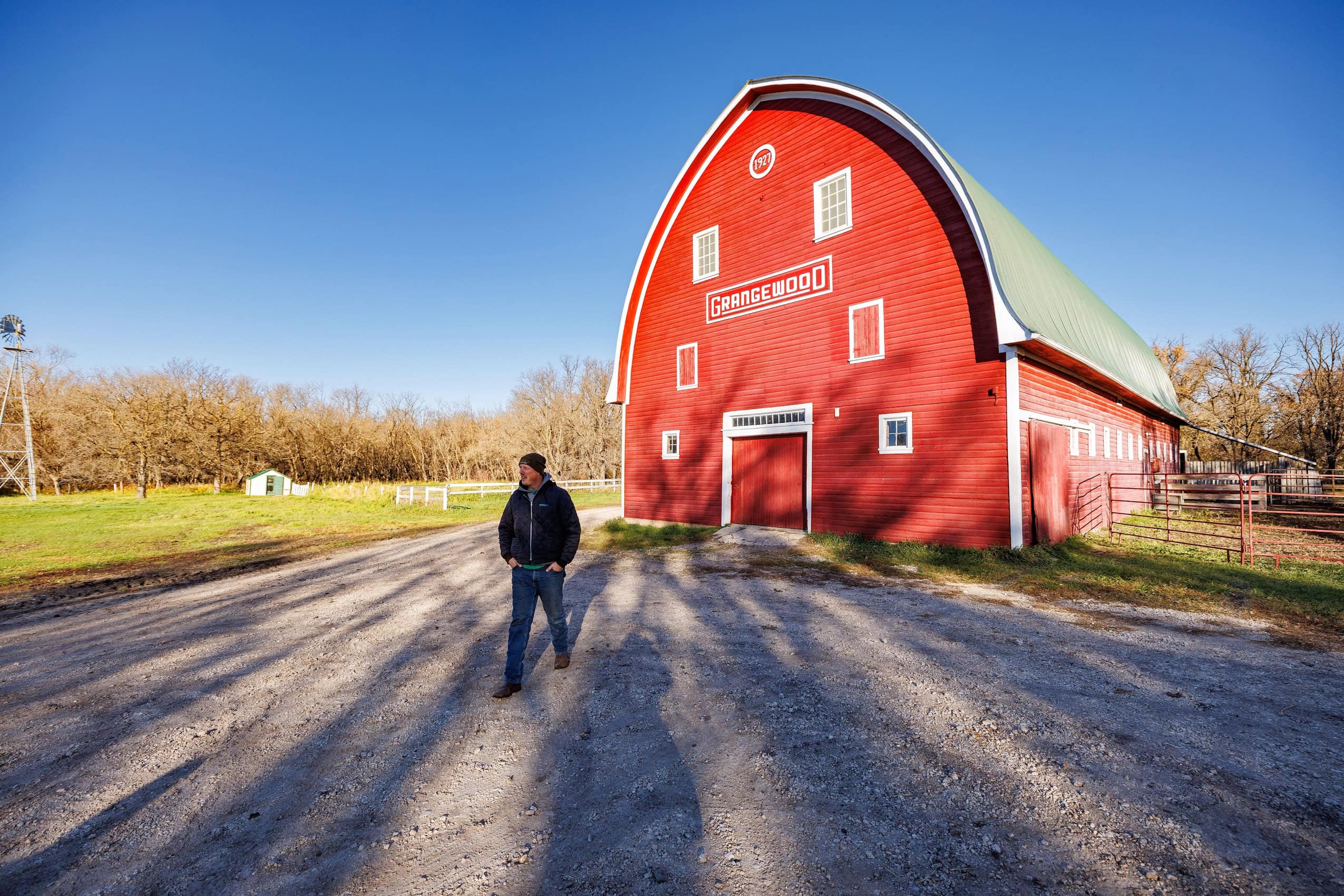 Nick Matheson walks in front a red barn on his farm in Manitoba a bright and sunny fall day.