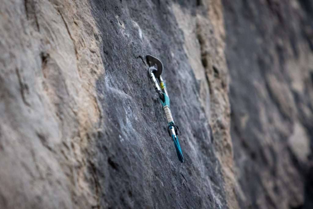 A closeup of a bolt affixed to the face of a cliff to aid in climbing. A climber's carabiner is hanging from it.