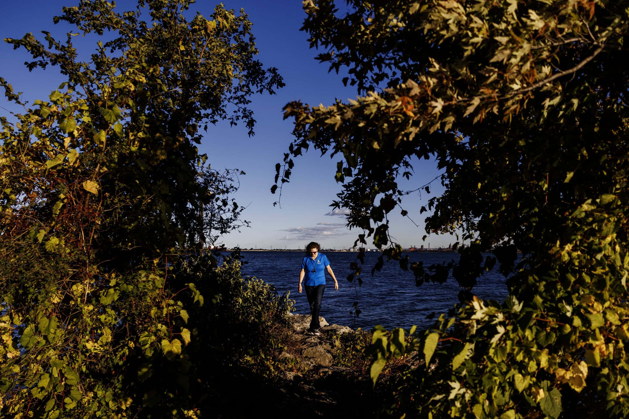Kristin O'Connor is photographed walking alongside Hamilton Harbour. She is framed by vegetation on both sides of her.