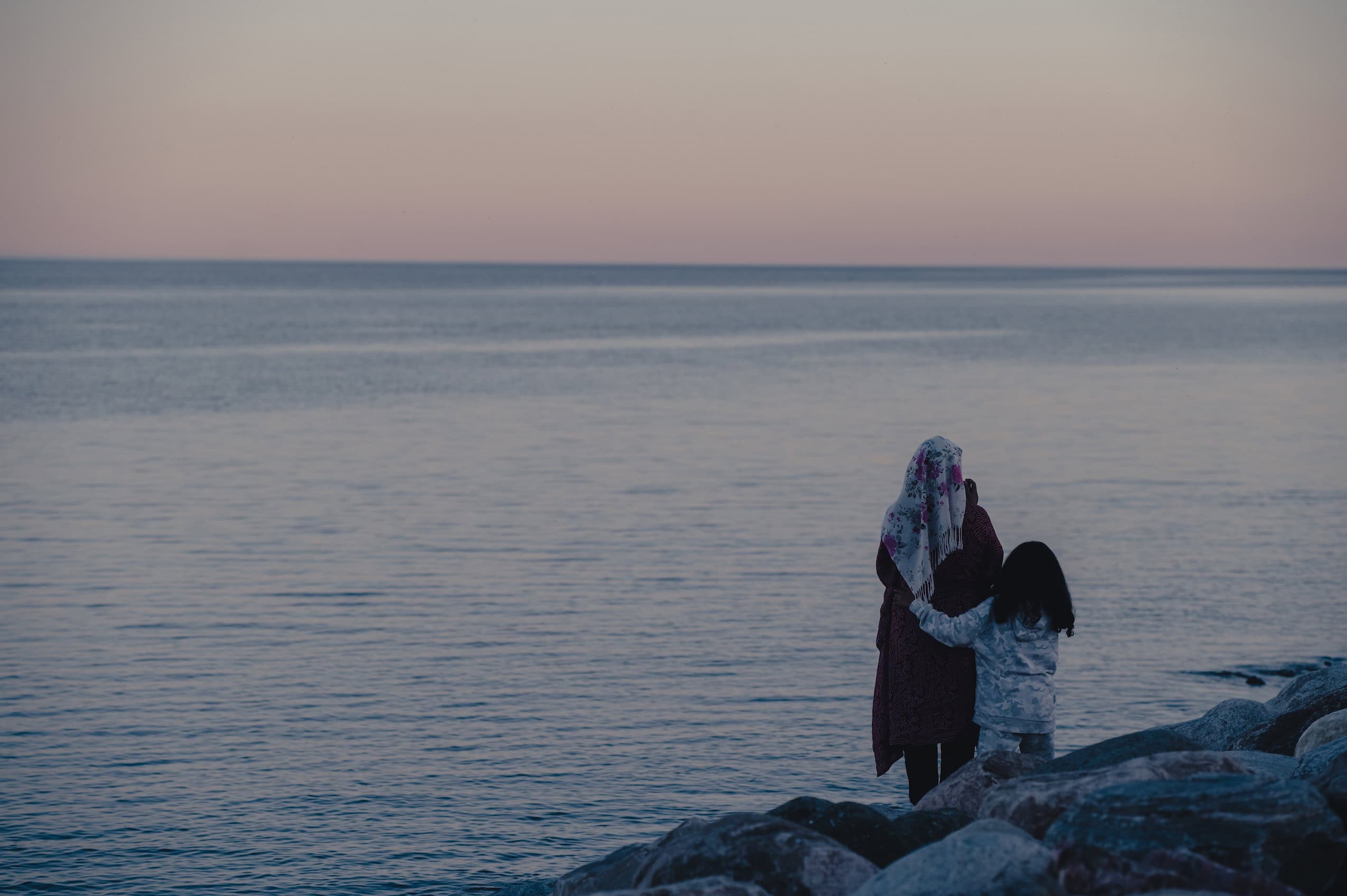 Two people, seen from behind, stand in front of Lake Ontario during twilight.