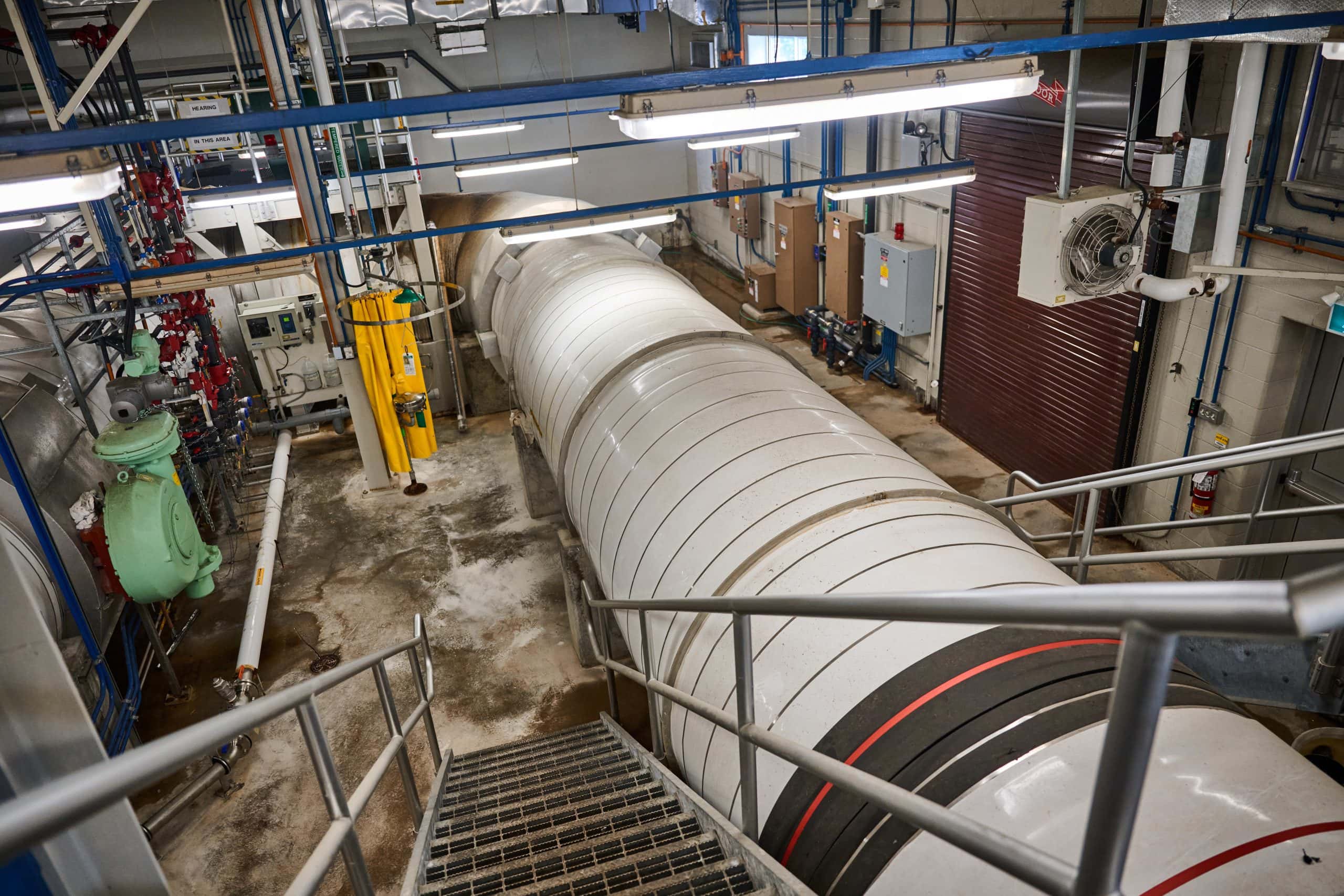 Large wide white pipe heading towards the wall inside an industrial looking room.