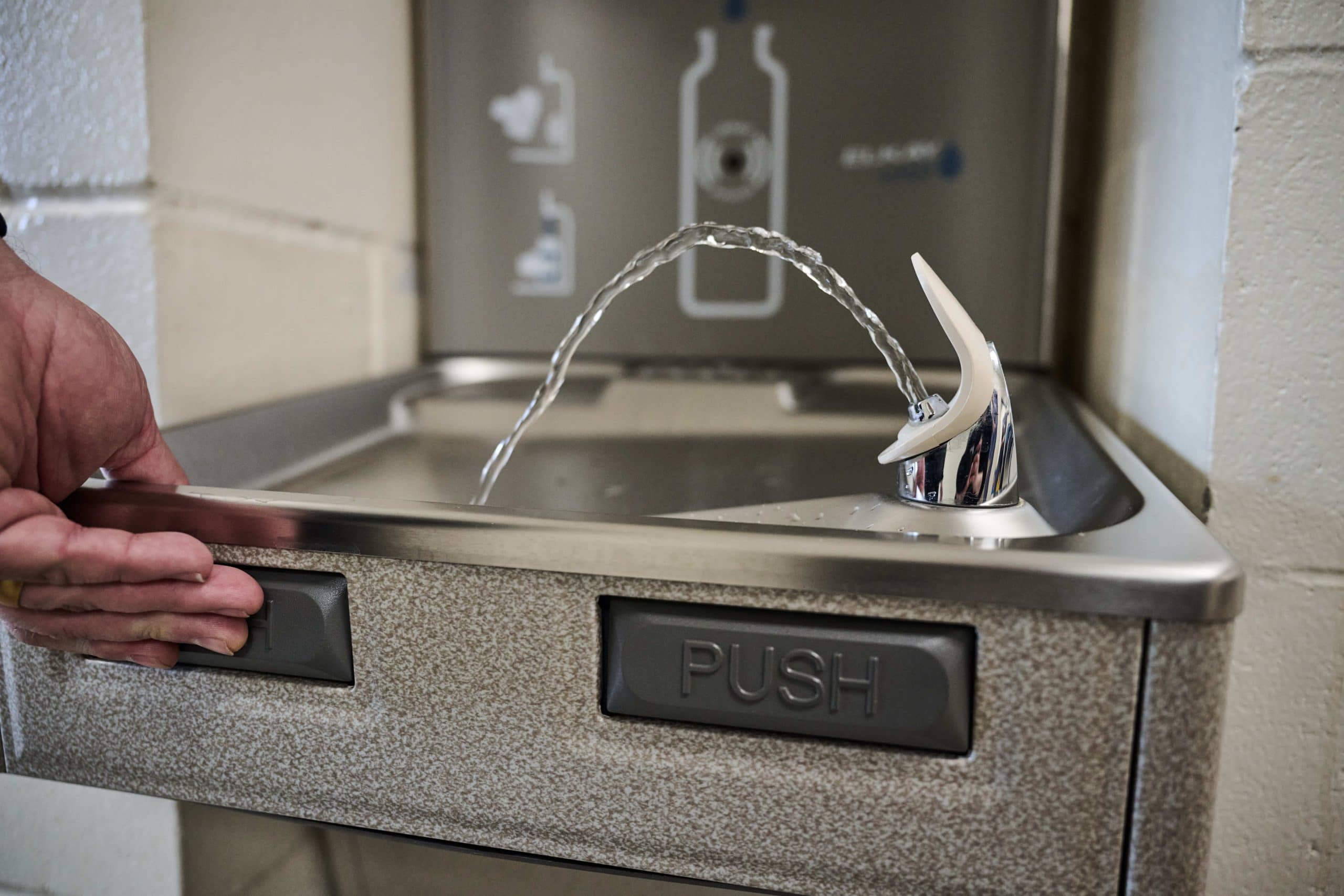 A hand presses the button on a water fountain.