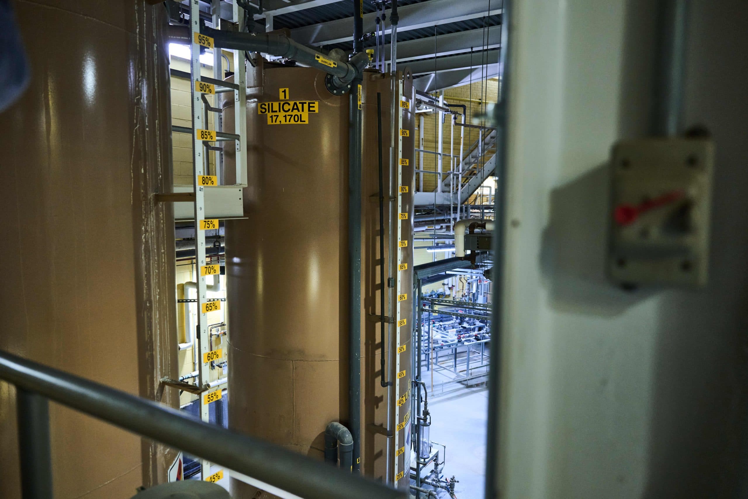 Large brown floor to ceiling tanks marked "alum" and "silica" in an industrial looking room.