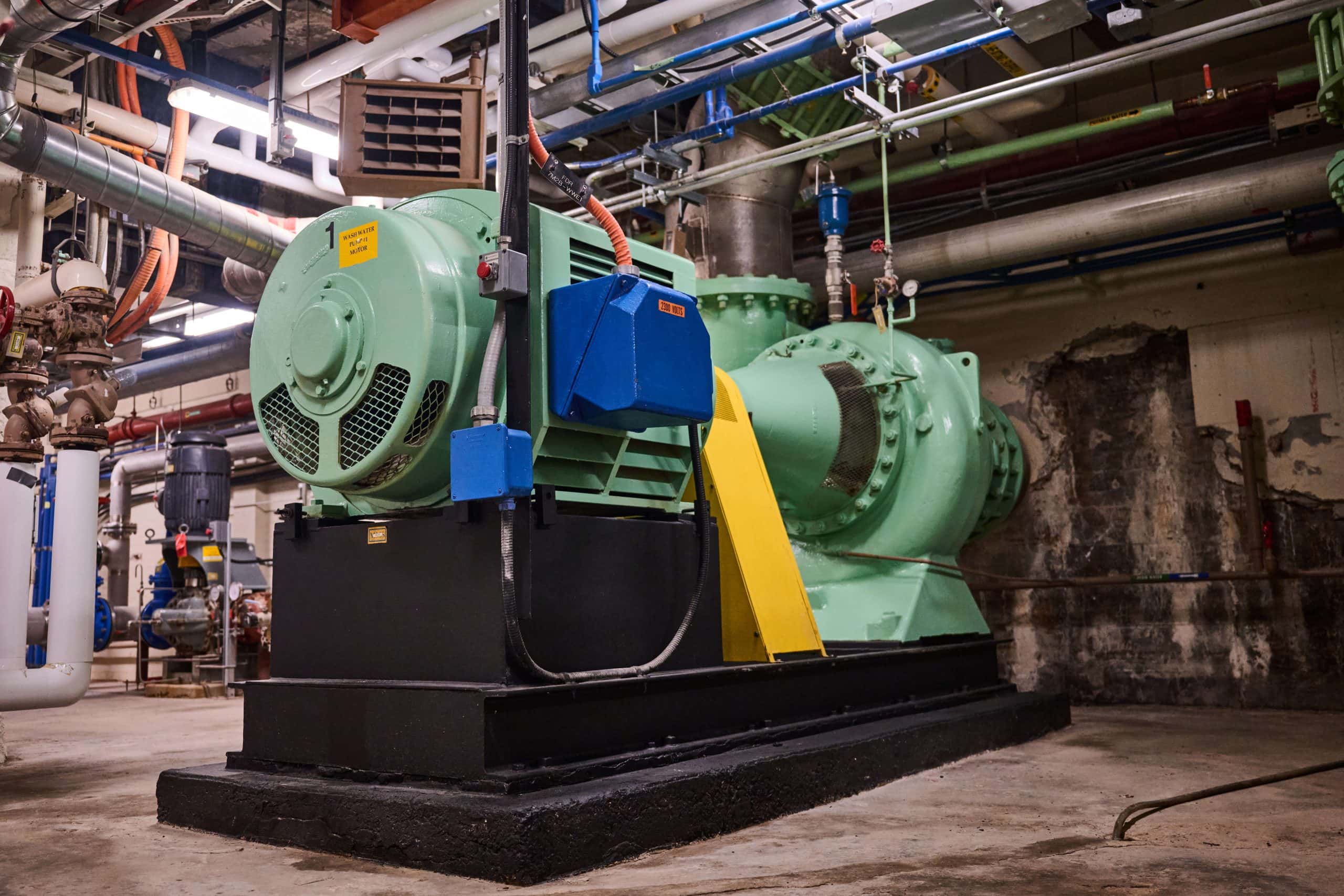 Large green painted pump sitting in a windowless concrete room.