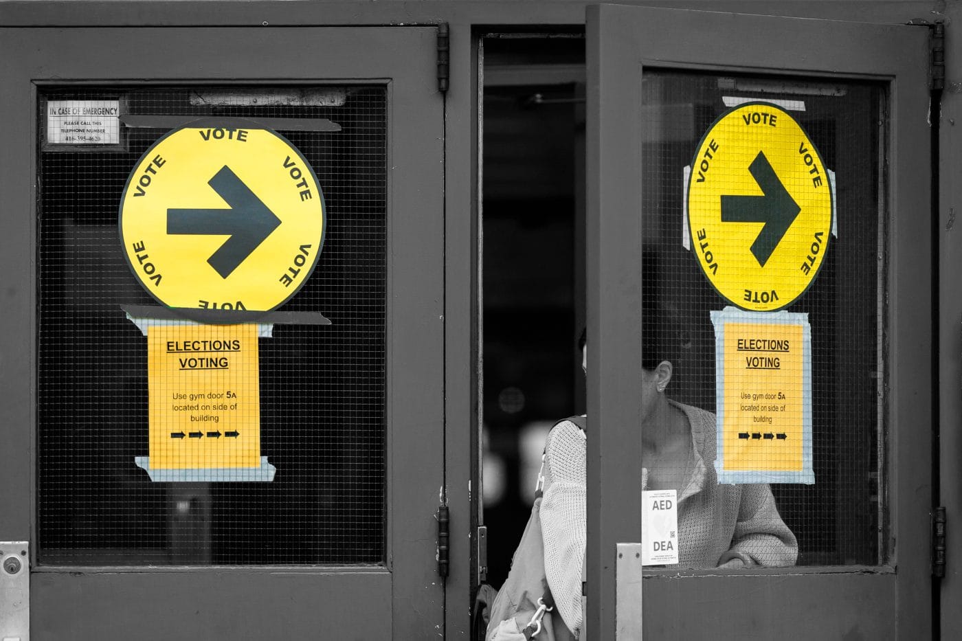 A person walks out of a building, the photo focuses on the doors with voting signs