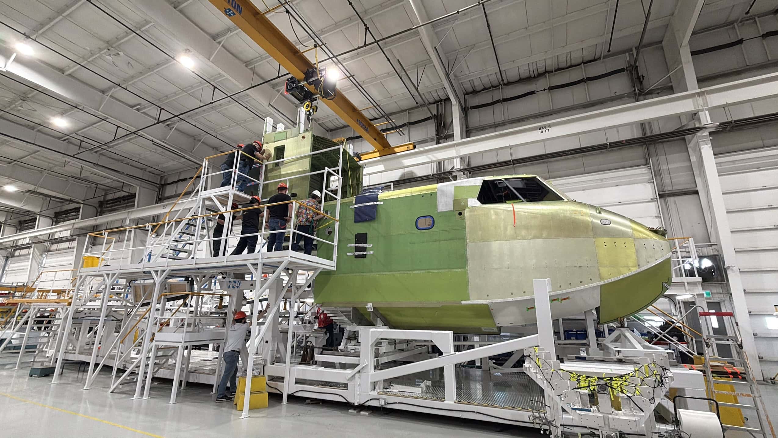 People wearing hardhats in a warehouse work on an unfinished water bomber aircraft.